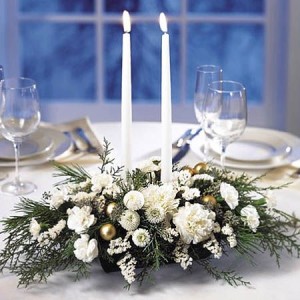 A Winter's Tale is an oblong design filled with assorted holiday greenery and all white flowers. Two white taper candles also included, creating the perfect tabletop setting.