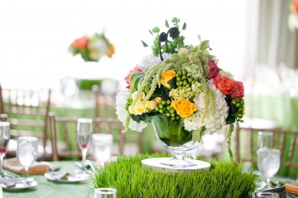 Glass pedestal vases filled with roses, hydrangea and amaranthus sit atop a base of green trick