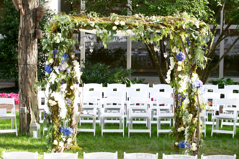 Birch chuppah with white sheer draping, natural greens and blue and white flowers