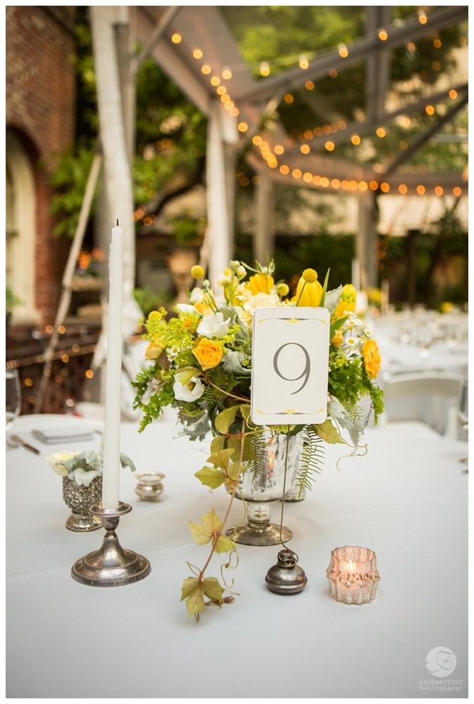 yellow and white flowers in a mercury glass vase with tapered candles and silver votives. 